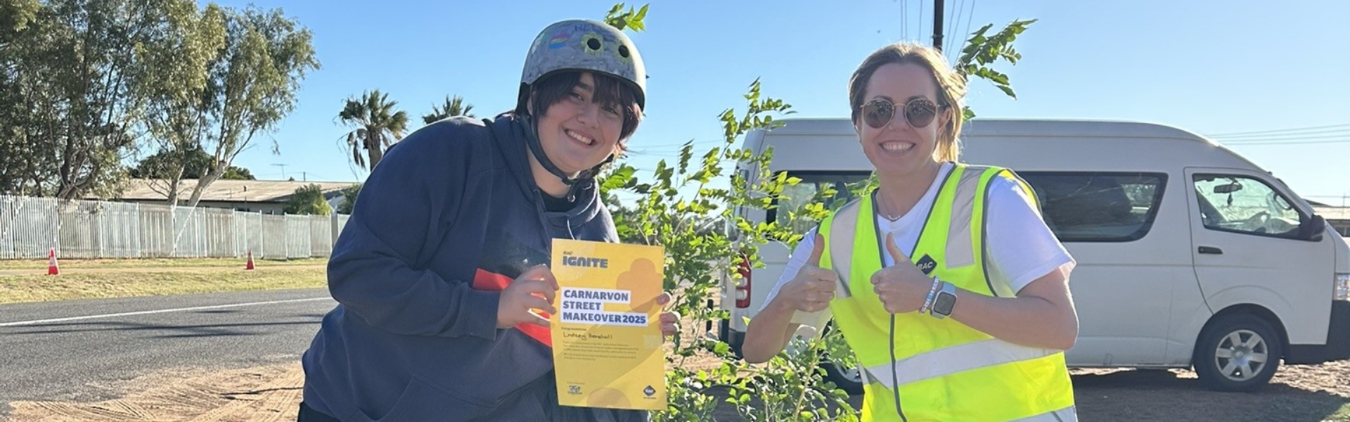 Two volunteers smiling at camera holding certificate in front of colourful plant in Carnarvon 
