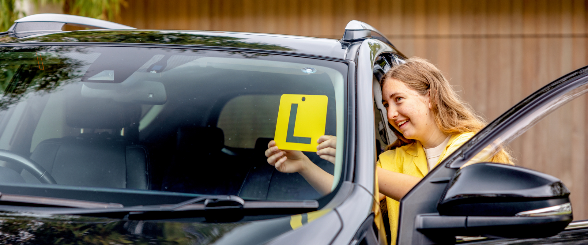 Young girl putting L plate on front window of car