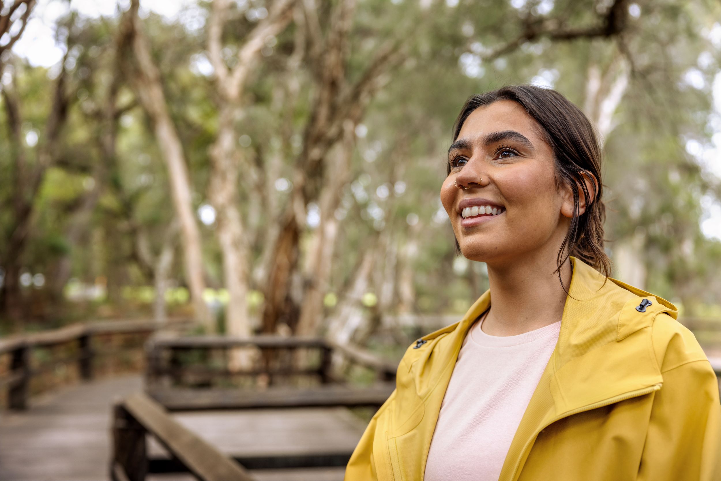 A young woman in a yellow rain jacket smiles as she walks in bushland
