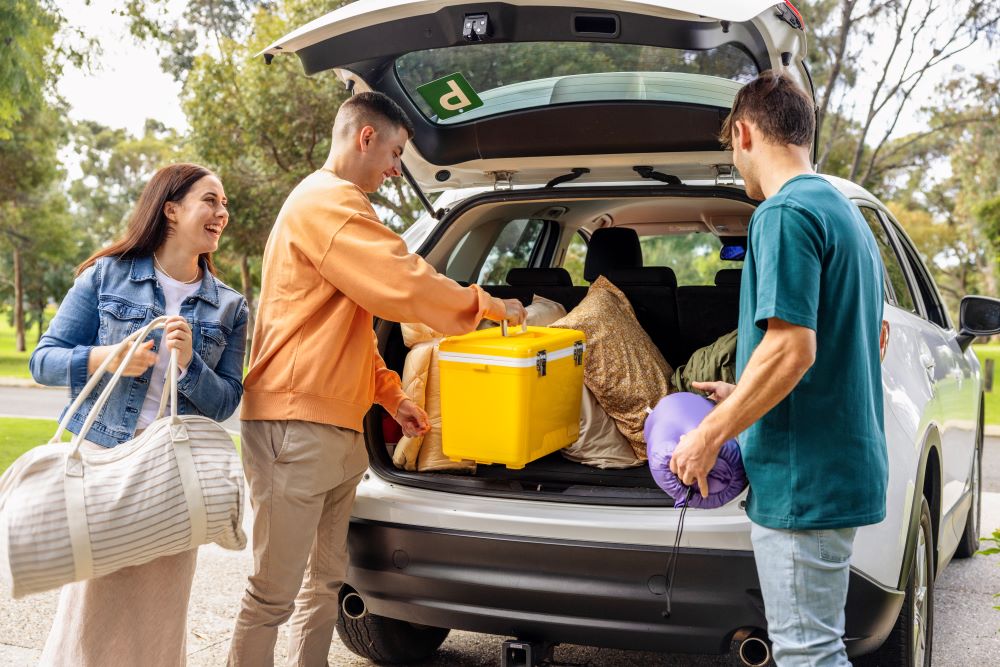 A group of young people smile and chat as they pack their car for a roadtrip