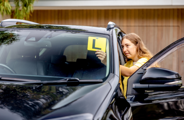 A learner driver attaching their L plates to their car.