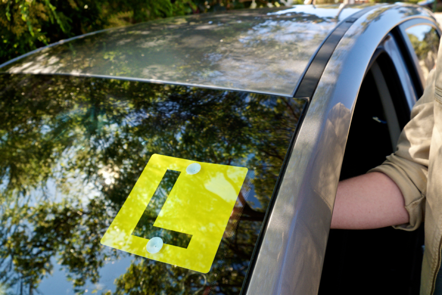Person putting L plates on the front window of a car
