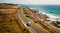 A motorhome is driving along the coast on a sunny day