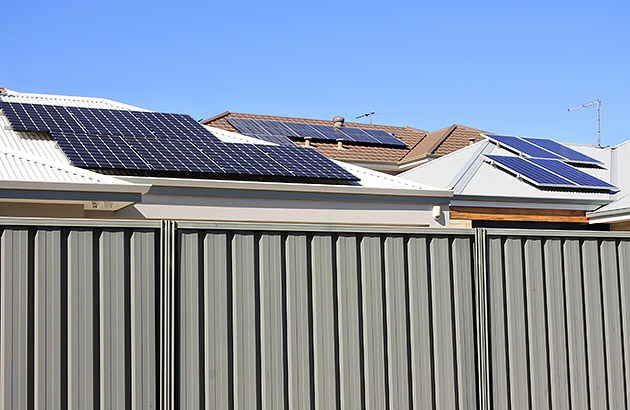 A cream Colourbond brand metal fence with house roofs visible behind it