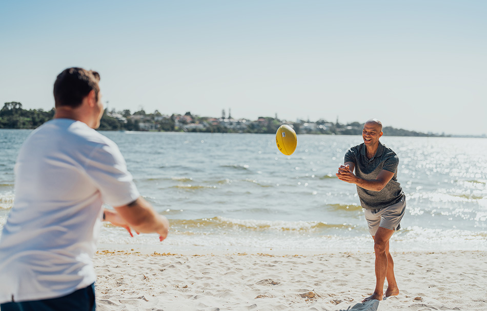 Two men are playing football together on the beach