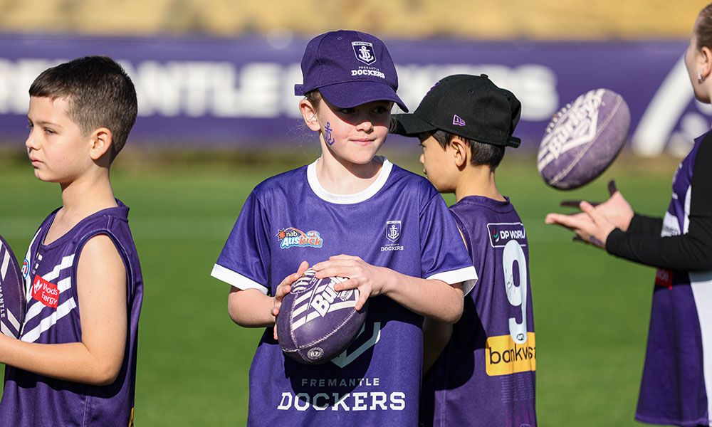 A group of children in Dockers jerseys are standing together holding footballs