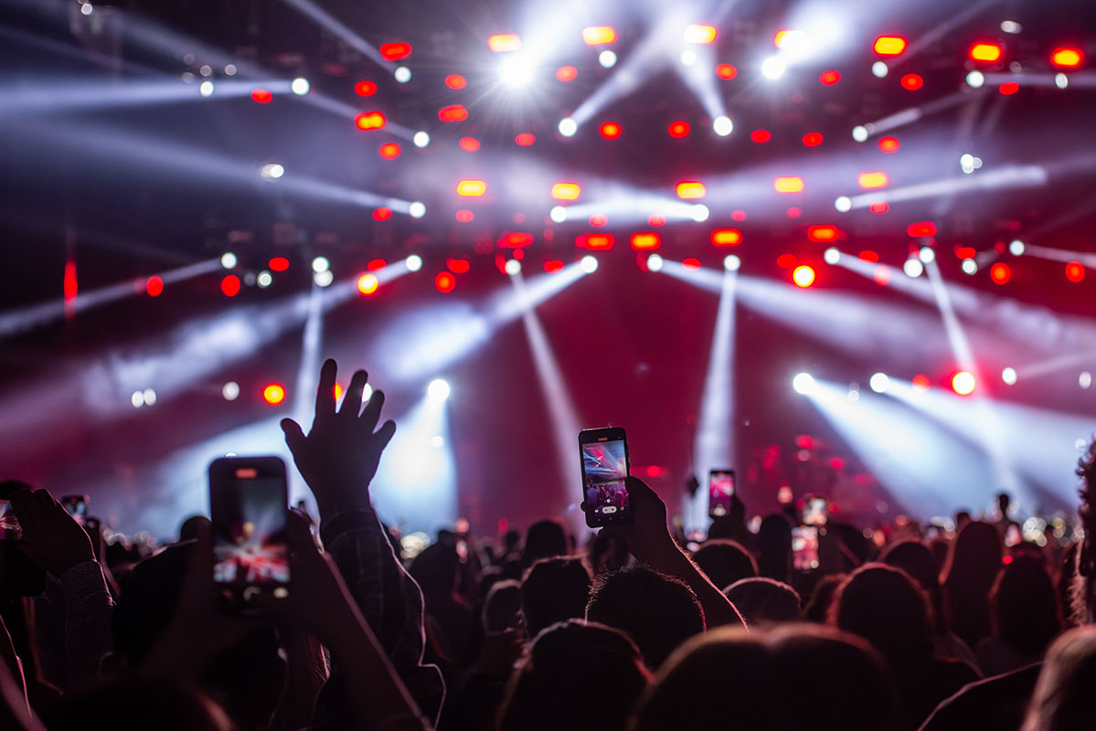 Huge concert with bright lights with people waving their hands and phones