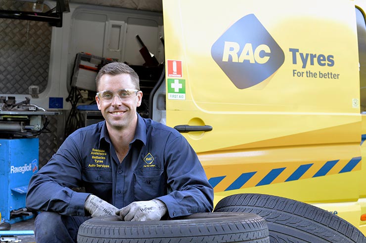 An RAC Tyres specialist crouches in front of the RAC Tyres van with car tyres in view