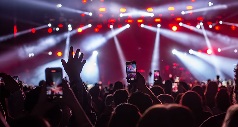 Huge concert crowd with bright lights and people waving their hands and phones