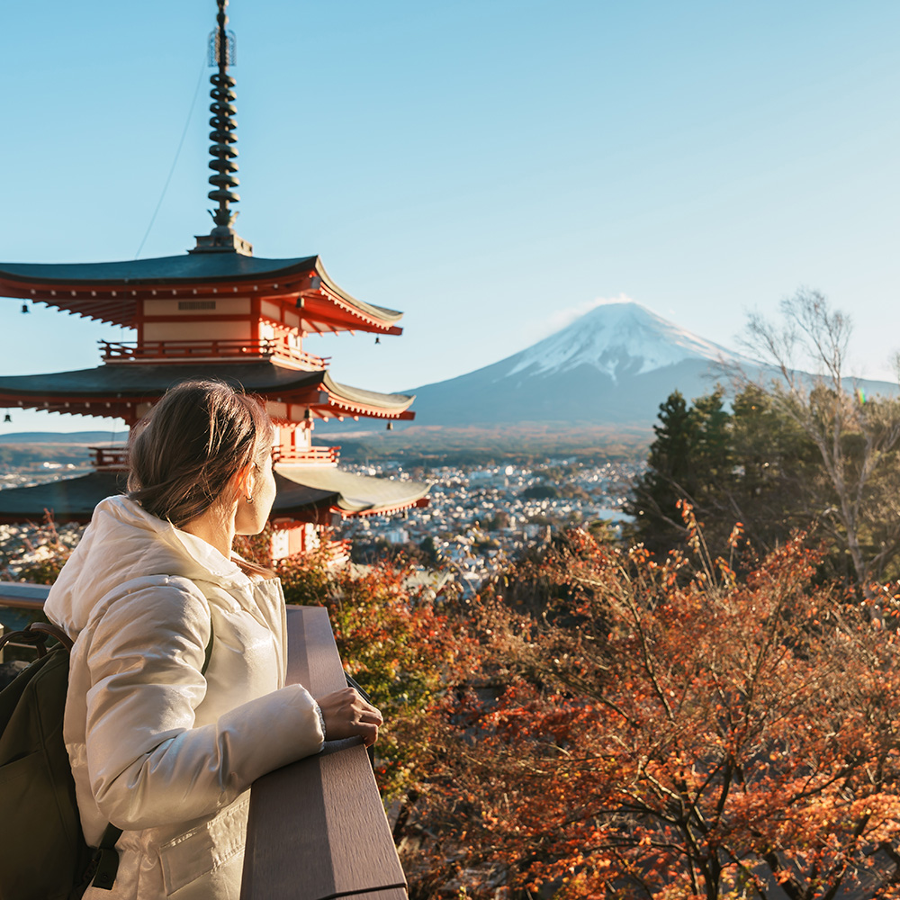 Lady standing on a balcony looking off at Mount Fuji.
