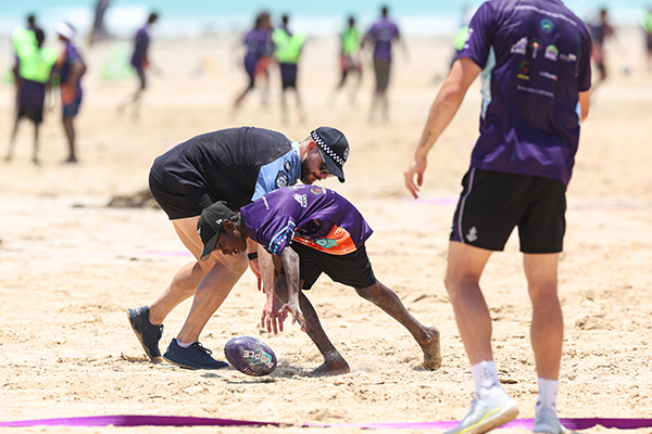 A young boy and a volunteer playing football on the beach sand.