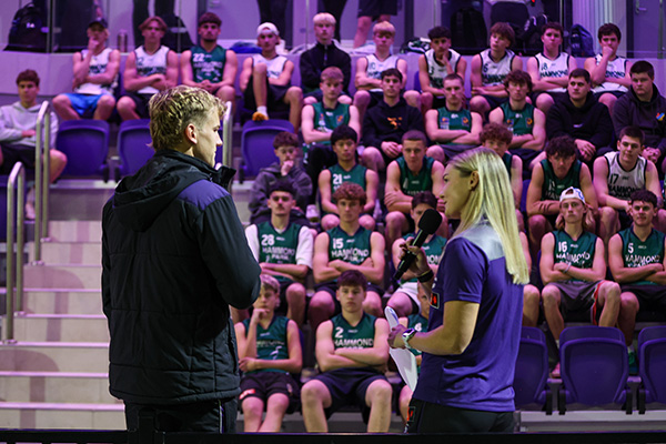 Male and female Fremantle football representatives standing on stage in from of many young footballers.