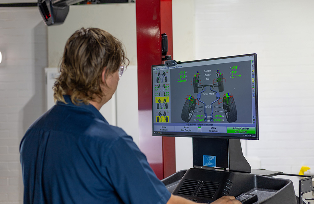 RAC Tyres technician operating a wheel alignment machine and viewing alignment data on a monitor in a workshop.