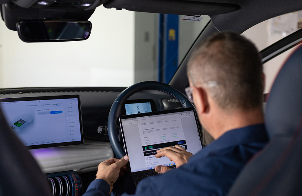 RAC mechanic inside an electric vehicle, reviewing EV battery health information on a tablet connected to the car.