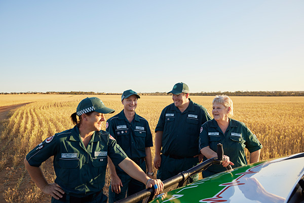 Four paramedics standing in front of the ambulance vehicle in a wheat field.