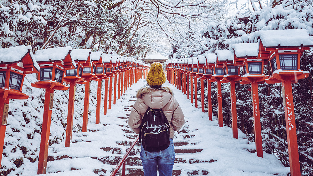 Lady walking up snowy stairs with red lanterns on either side.