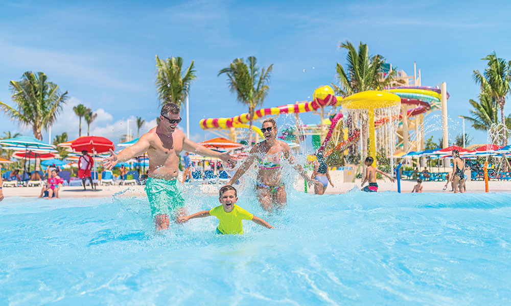 A man and a woman are running into a pool laughing, with a young boy in the front