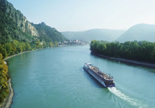 A river ship cruising down the river flowing between green hills 