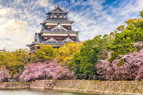 A tall shrine peering over some pink cherry blossoms in Japan