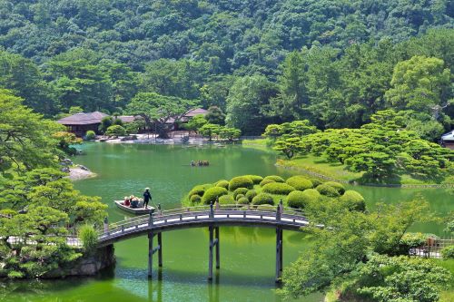 A green lake surrounded by lush green trees with a bridge arching over 