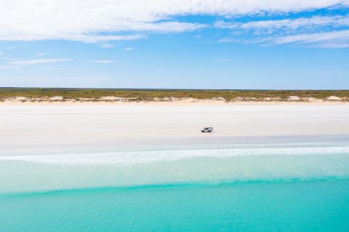 A 4WD driving on white sanded Cable Beach with the vibrant turquoise ocean next to it. 