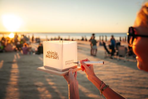 Close up of a Shinju lantern and a lively beach event at sunset in the background. 