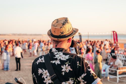 Musician performing at a lively beach event during sunset, with a crowd gathered in the background.