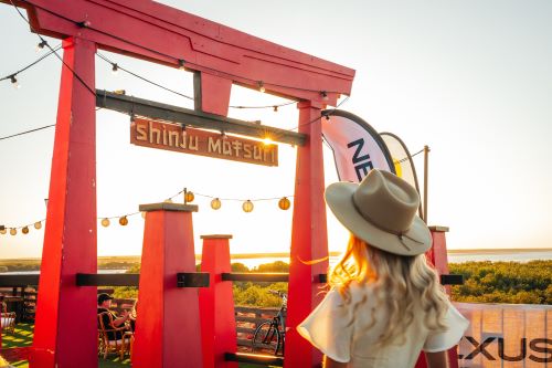 Woman walking toward the red Torii gate entrance of Shinju Matsuri festival at sunset.