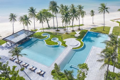 Aerial view of the pool area located directly by the beach surrounded by palm trees.