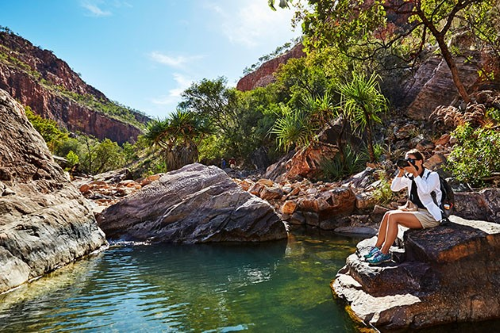 A tourist sitting by the water at Emma Gorge taking photos
