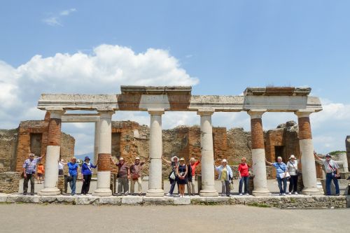 Group of visitors standing among ancient stone columns and ruins at Pompeii under a bright blue sky.