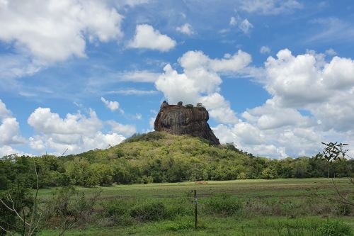 Sigiriya Rock rising above green countryside under a blue sky filled with large white clouds, Sri Lanka.