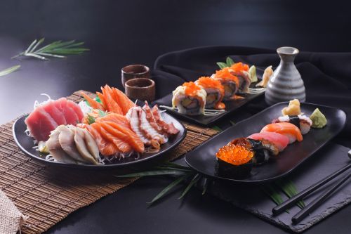 Assorted Japanese sushi and sashimi platters served on black plates, with salmon, tuna, seafood rolls, wasabi and a sake carafe.