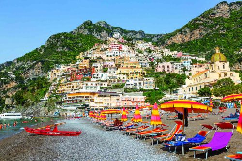 Colourful beach umbrellas and loungers on a pebble beach below Positano's hillside village on Italy's Amalfi Coast.