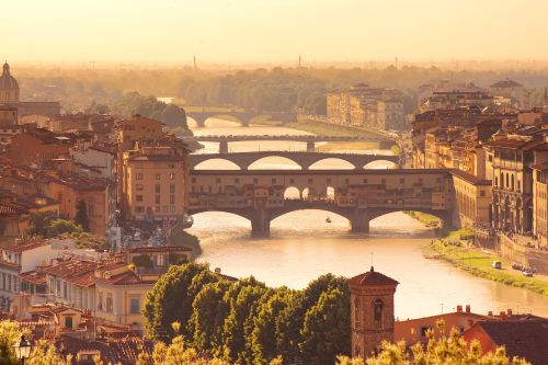 Sunset view of Florence, Italy, with the Ponte Vecchio spanning the Arno River and historic buildings lining the riverbanks.