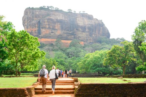 Visitors walking towards the base of Sigiriya Rock through landscaped gardens and ancient stone pathways, Sri Lanka.