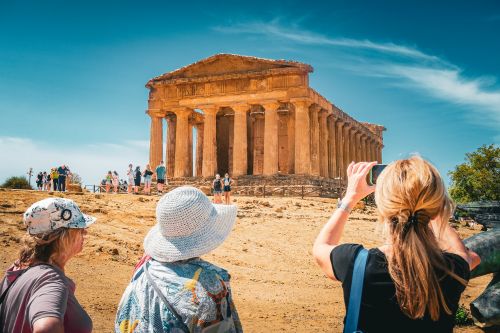 Visitors viewing an ancient Greek temple in Sicily under a clear blue sky.