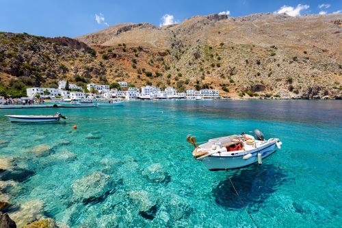 Clear blue waters in Greece surrounded by mountains and a small boat in the foreground 