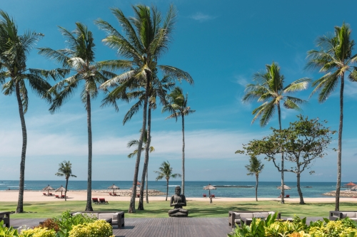 A buddha stature sitting close to the palm tree lined sea front