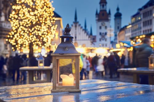 Close-up of a candle lantern with a church and Christmas tree in the background. 