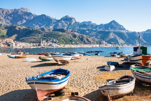 Boats on urban beach in Giardini Naxos town with mountains in the background. 
