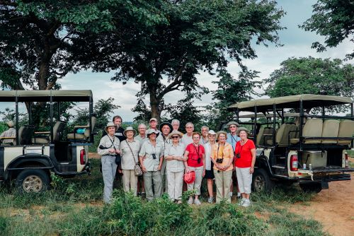 The whole group standing between two safari jeeps and smiling for a photo.