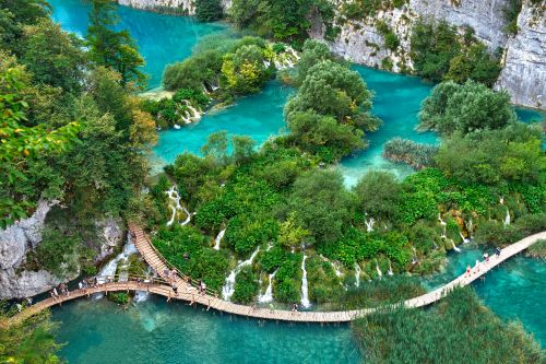 Turquoise lakes and cascading waterfalls at Plitvice Lakes National Park, with wooden boardwalks winding through lush green forest.