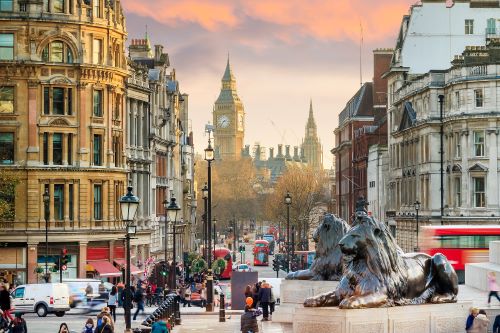 View of Big Ben from Trafalgar Square with people and traffic in the foreground at sunset.