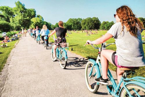 A group of young travellers push biking through the park 