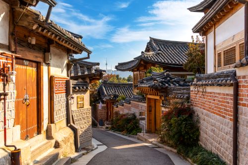 A street lined with traditional Korean houses creating a contrast to the modern skyline of Seoul visible in the background 
