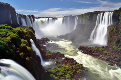 Wide view of Iguazu Falls with multiple waterfalls cascading into a mist-filled river gorge.