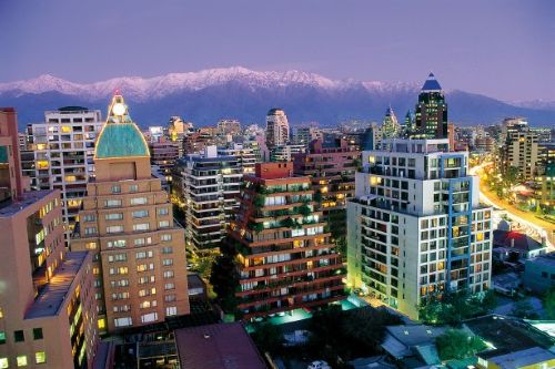 City skyline at dusk with modern buildings and snow-capped mountains in the background.