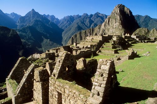 Machu Picchu ruins with stone terraces set against steep green mountains under a clear blue sky.