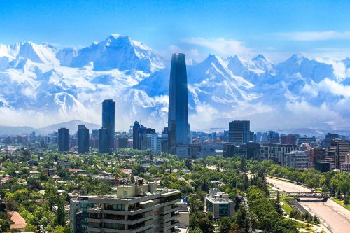 Santiago skyline with modern high-rise buildings in the foreground and snow-capped Andes mountains in the background under a clear blue sky.